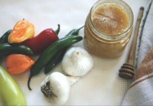 Fermented garlic jalapeño hot honey flat lay with peppers, garlic, and a bubbling jar of honey