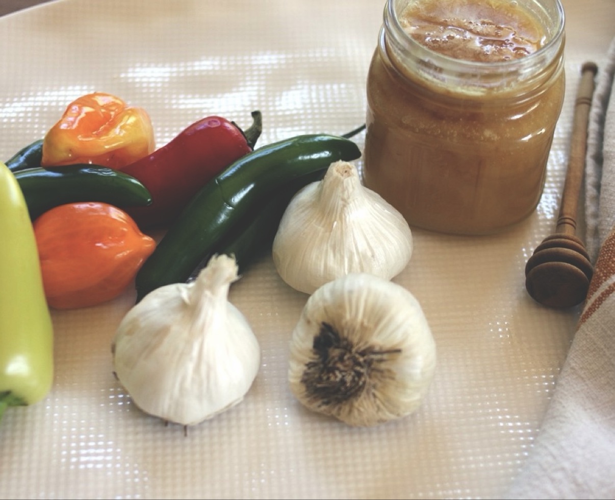 Ingredients flat lay for fermented garlic jalapeño hot honey: habaneros, serrano, jalapeño, garlic, and raw honey