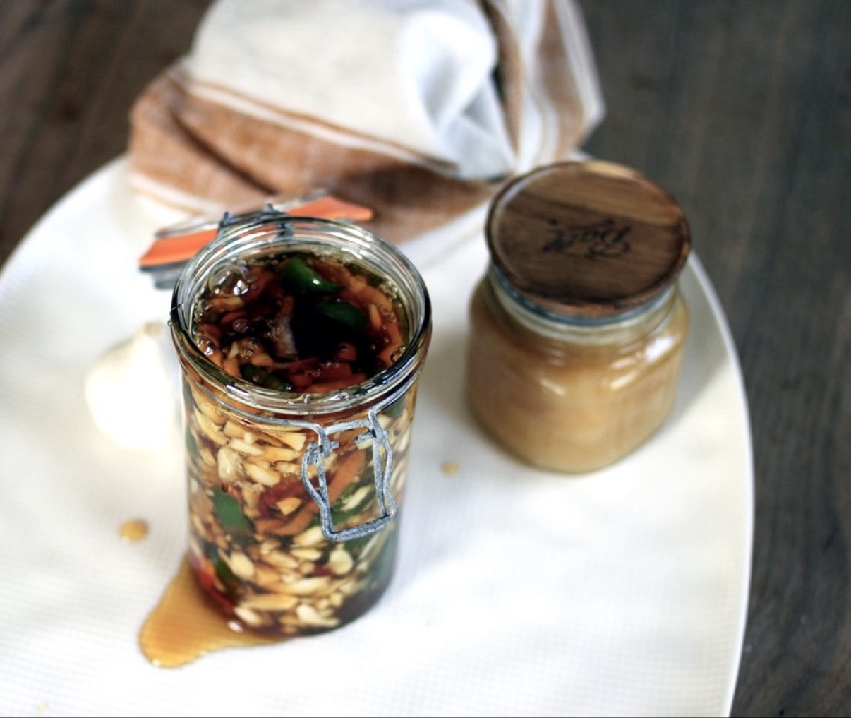 Overhead view of a jar of fermented garlic jalapeño honey next to a honey pot, ready to drizzle