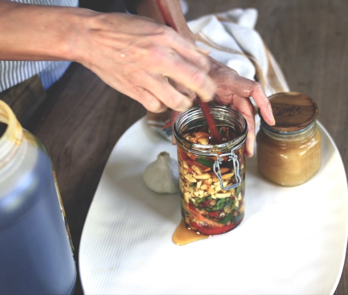Stirring fermented garlic jalapeño honey in a jar to release air pockets after pouring honey over sliced peppers and garlic